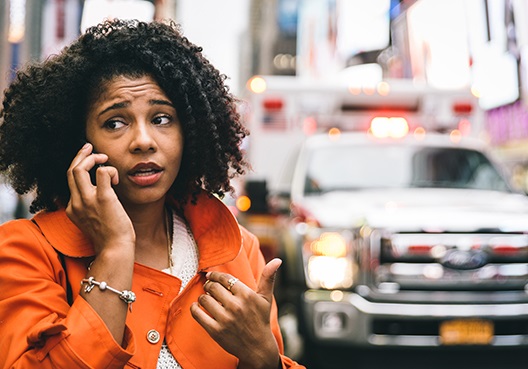 A woman on her cellphone with an ambulance pictured in the background